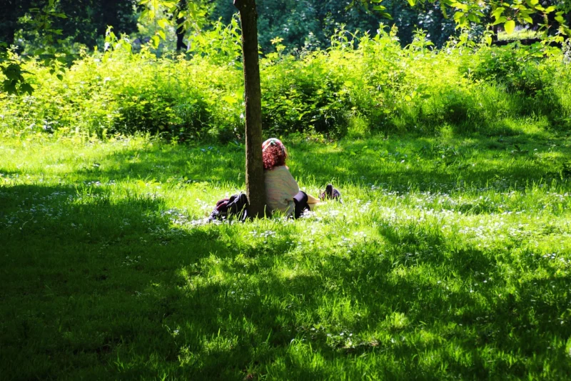 Mlada žena tiho sedi na travi u zelenom parku, izgleda smireno i zaokupljeno sobom u meditaciji