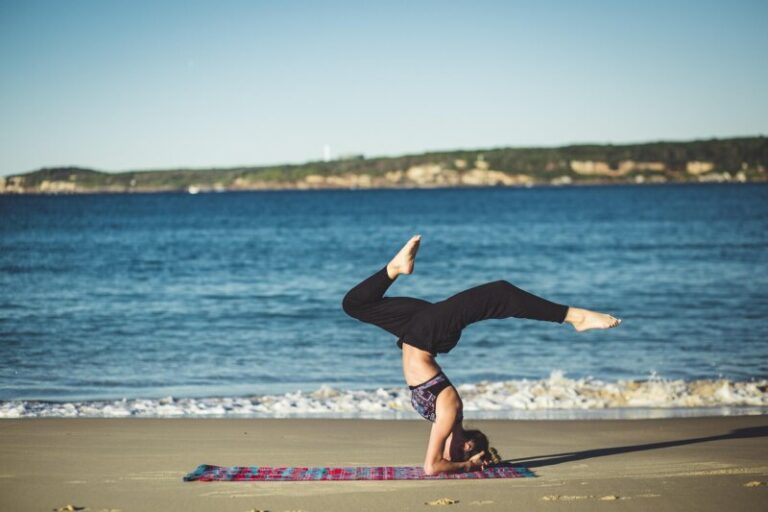 Žena sedi u pozi meditacije na peskovitoj plaži uz mirno plavetnilo okeana