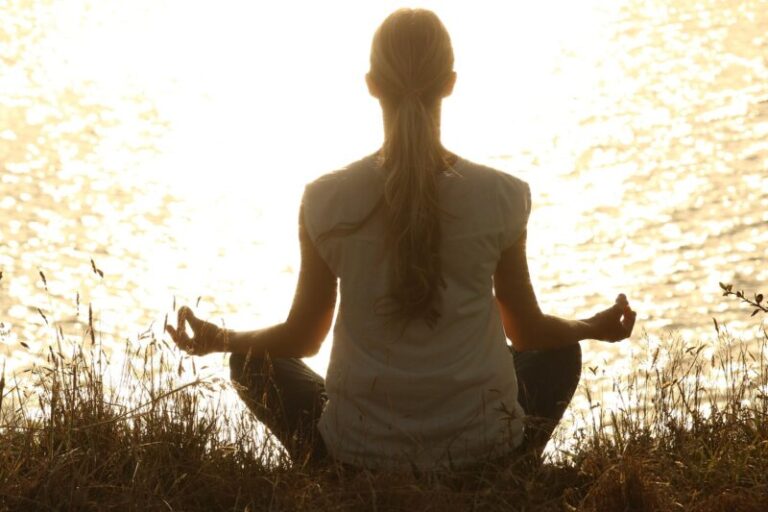 silhueta žene koja meditira u prirodi tokom zalaska sunca