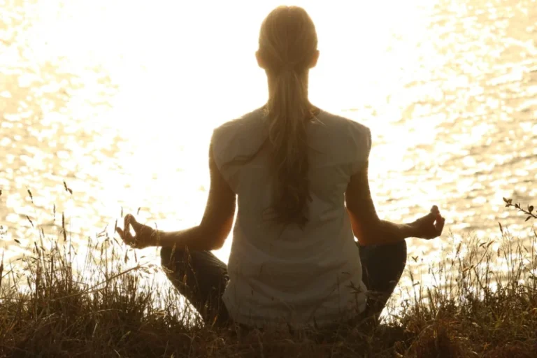Žena meditira u prirodi tokom zalaska sunca, sedeći u joga pozi na travi, okružena spokojem i tišinom