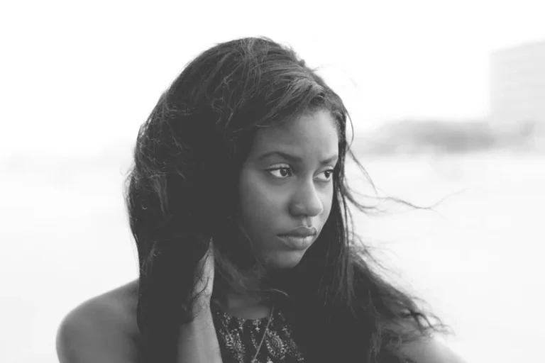 Crno-bela fotografija mlade Afroameričke žene sa zamišljenim i tužnim izrazom lica na vetrovitom danu