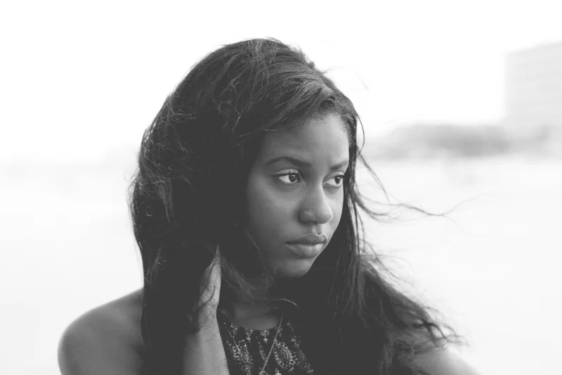 Crno-bela fotografija mlade Afroameričke žene sa zamišljenim i tužnim izrazom lica na vetrovitom danu