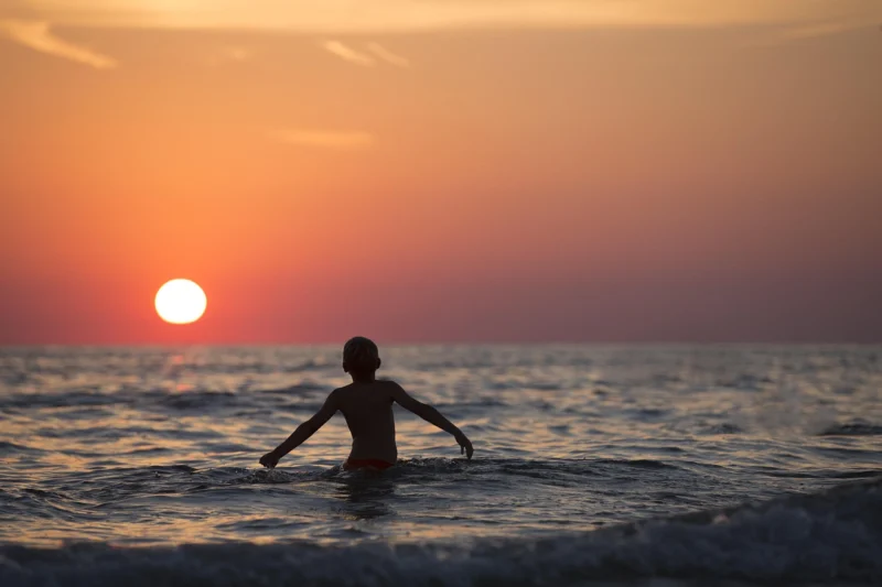 Silhueta dečaka koji stoji na plaži dok sunce zalazi na horizontu
