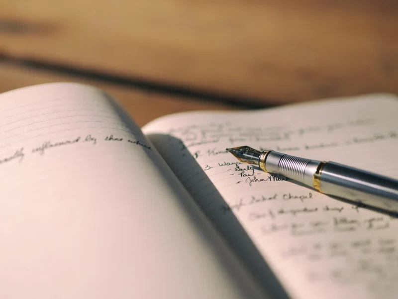 Osoba koja piše beleške u notes sa nalivperom na drvenom stolu