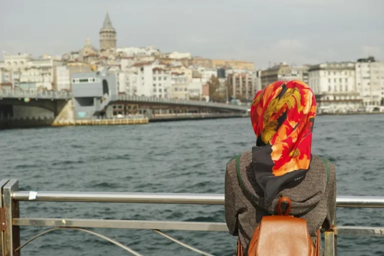 Mlada žena sedi sama na obali mora u Istanbulu, zamišljeno gleda u daljinu prema horizontu, dok joj vetar nežno pomera kosu